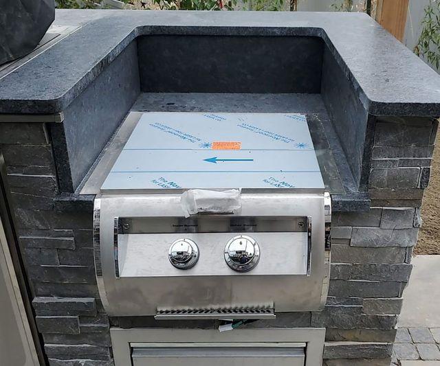 Granite outdoor kitchen countertop surrounding a built-in grill opening being evaluated for replacement